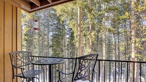 Un espace extérieur abrité, avec des chaises et une table en métal, donnant sur une zone boisée où se dressent de grands arbres.