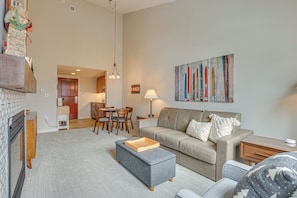 A living room with a sofa, ottoman, and a dining area with chairs and a table. - Mtn Views & Pool Access: Sunny Winter Park Retreat (Winter Park)