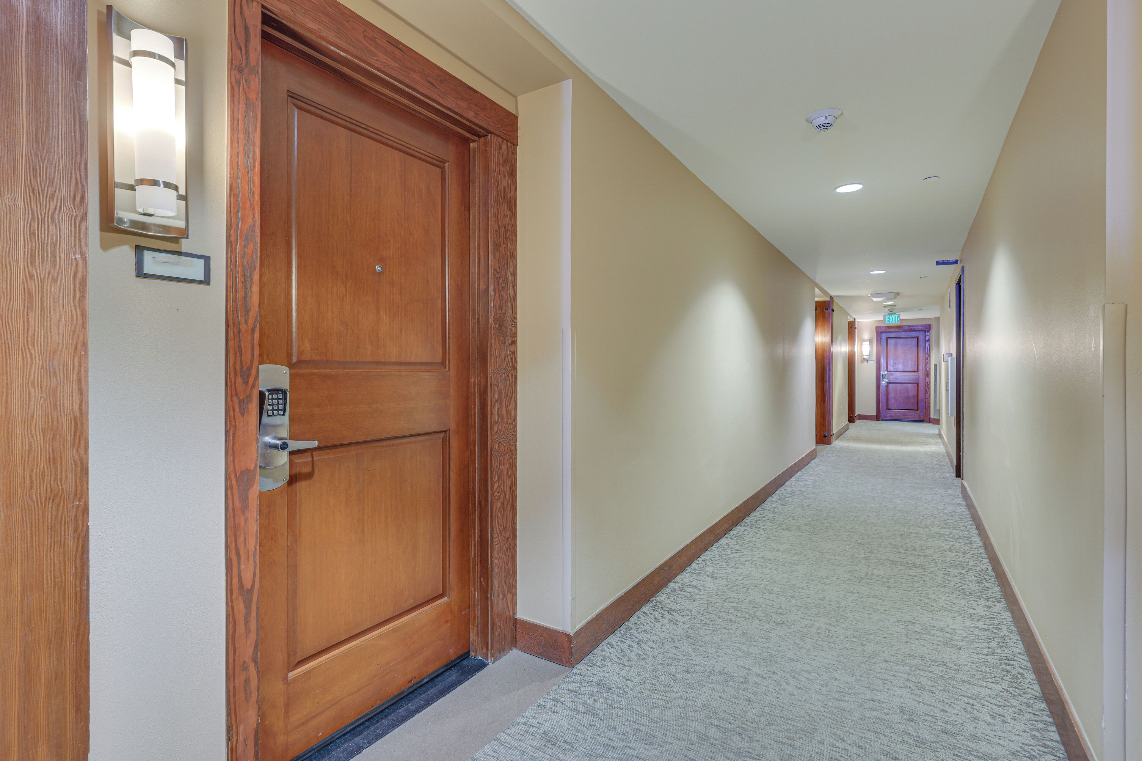 A hotel hallway with a wooden door, a light fixture, and a carpeted floor.