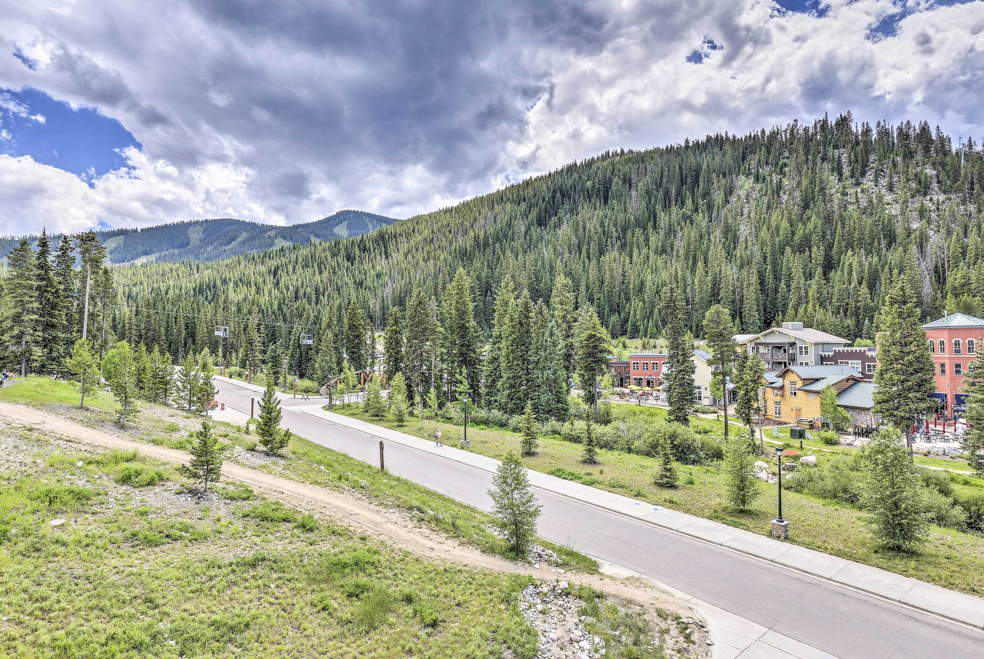 A road leading to a town with buildings and a forested mountain in the background.