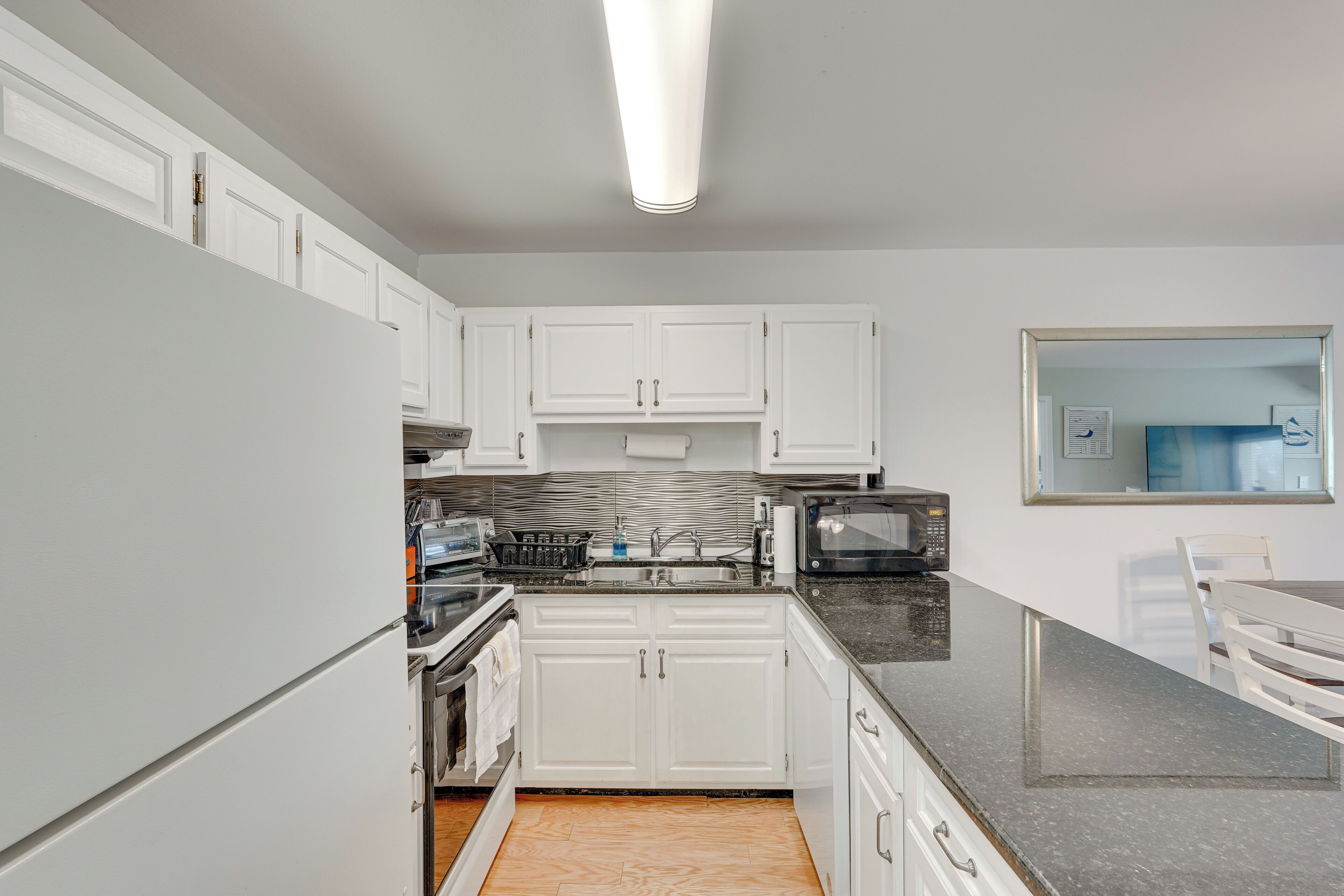 A modern kitchen with white cabinets, a granite countertop, a microwave, and a sink.