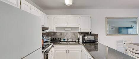 A modern kitchen with white cabinets, a granite countertop, a microwave, and a sink.