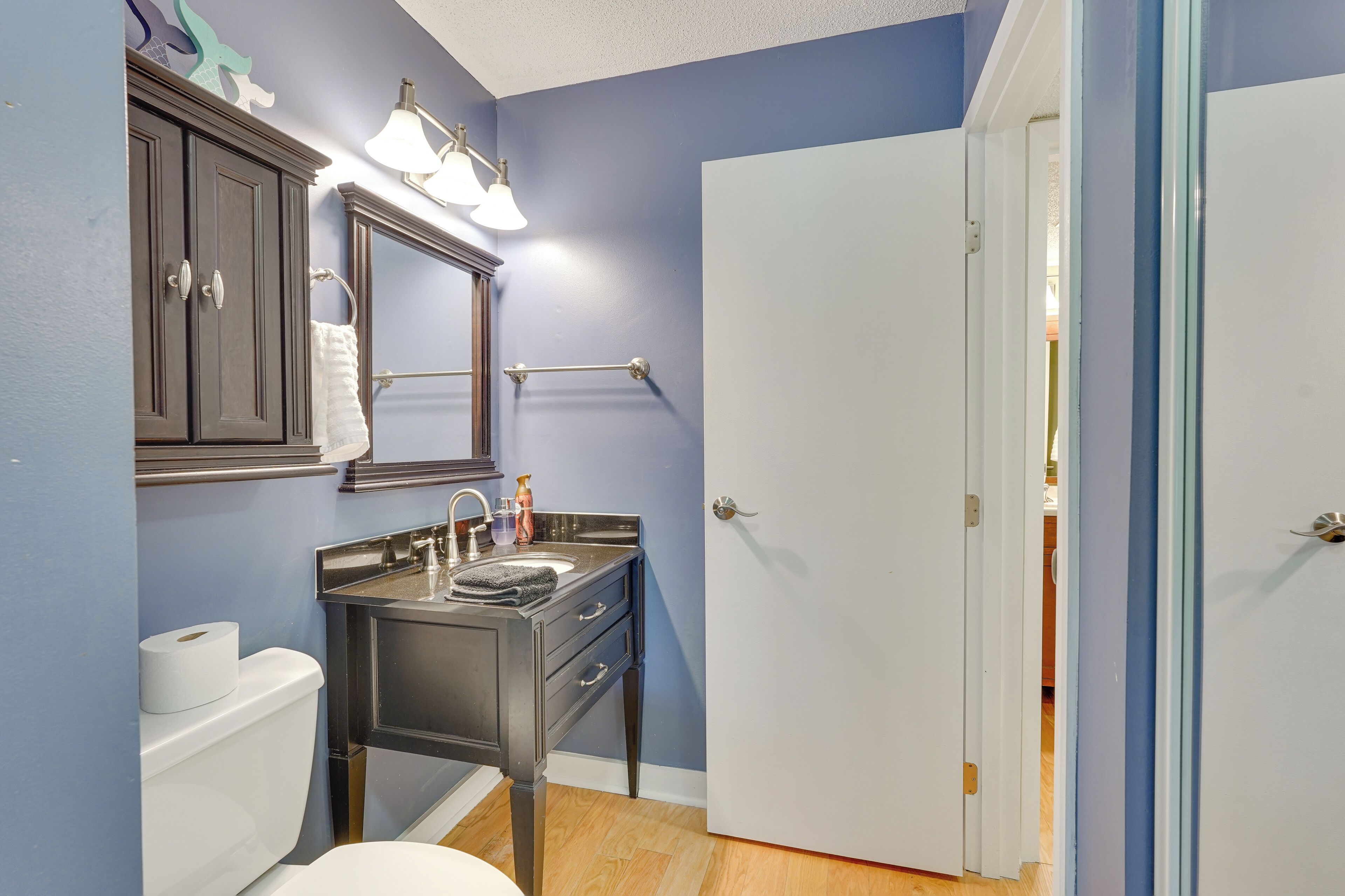 A bathroom with a dark vanity, a white toilet, a towel rack, and a door leading to another room.