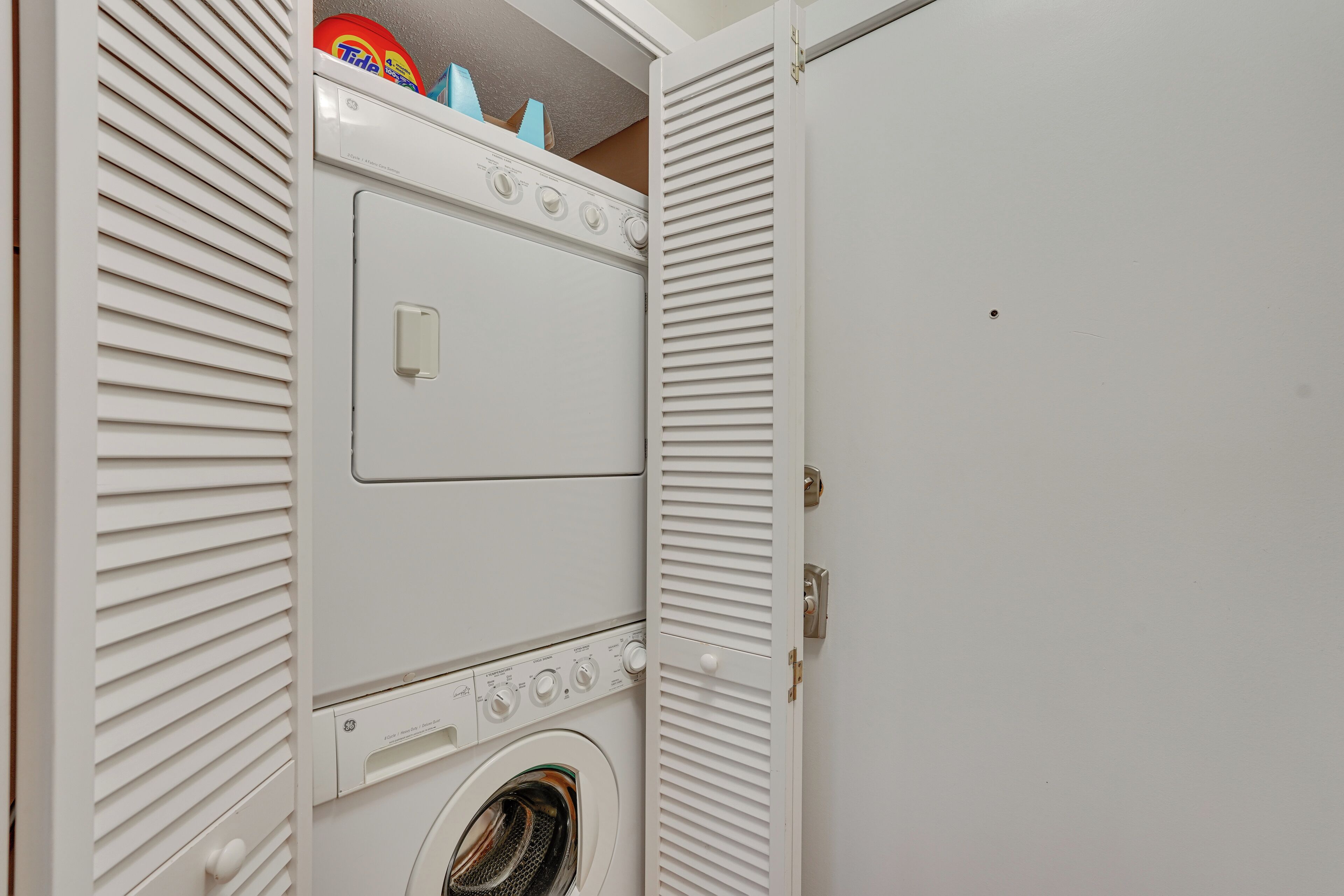 Une petite buanderie équipée d’un lave-linge à chargement frontal, d’un sèche-linge et d’une étagère au-dessus du lave-linge.