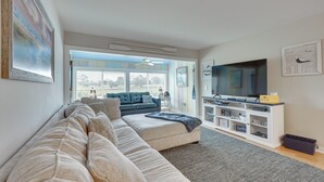 Una sala de estar con un amplio sofá beige modular, un televisor de pantalla plana y un mueble blanco para entretenimiento.