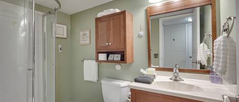 A bathroom with a shower, toilet, vanity, and a mirror.