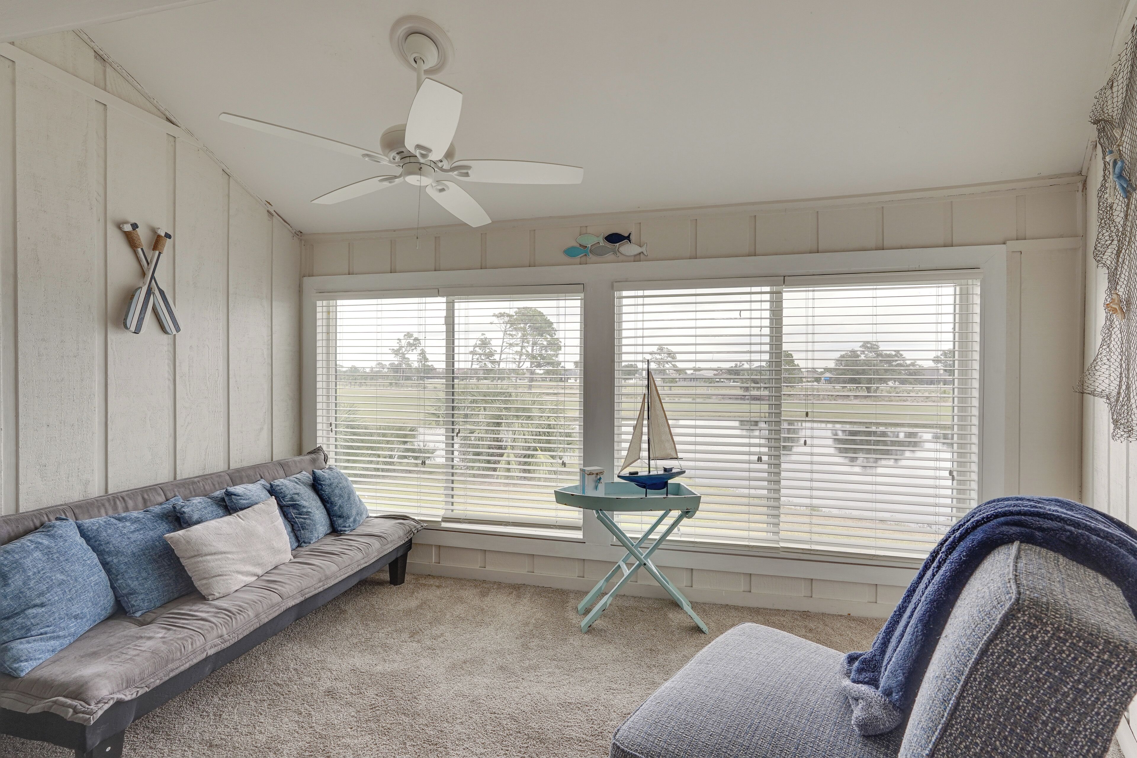 A room with a gray sofa, a small table with a sailboat model, and a ceiling fan.