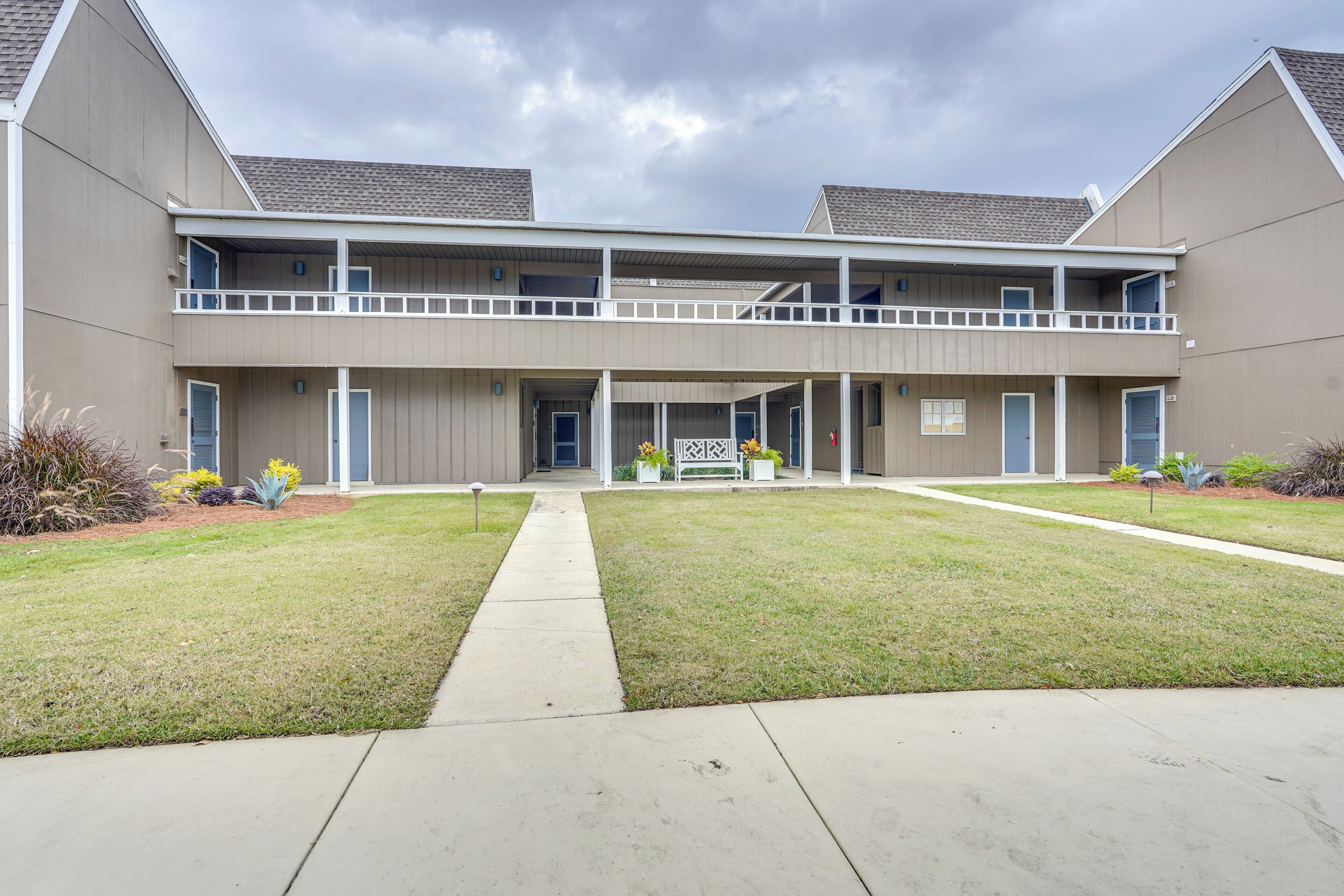A two-story building with a central entrance, a covered walkway, and a small garden area with plants and flowers.