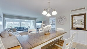 Un salón amplio con una mesa de comedor de madera, sillas blancas, un sofá y un ventanal que proporciona luz natural.