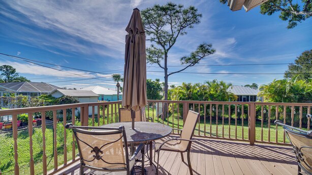 A wooden deck with a table and chairs, an umbrella, and a view of a residential area with houses and trees. - Sebastian Home w/ Large Deck Near Golfing & Beach (Sebastian)