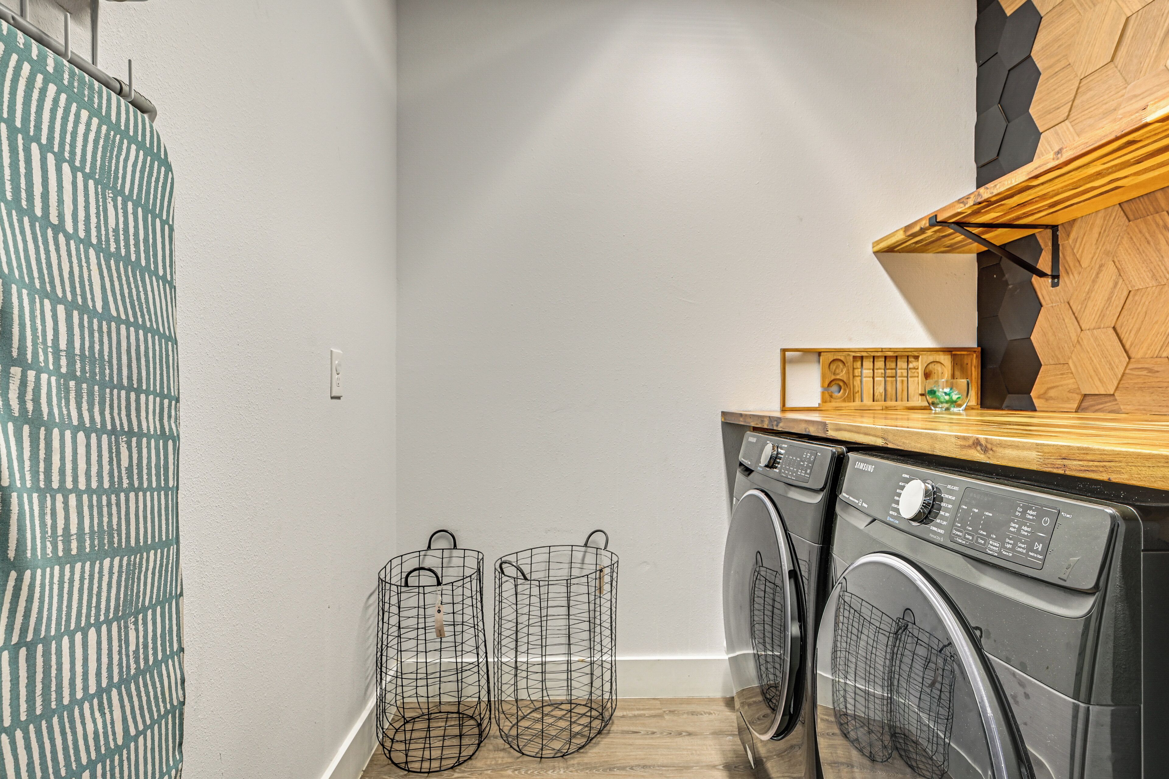 A laundry area with two washing machines, a wooden countertop, and two wire baskets.