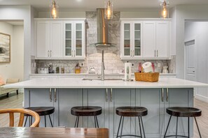 A modern kitchen with white cabinets, a large island with stools, and pendant lighting. - Modern Home Pet Friendly Kids Playroom More! (Lutz)
