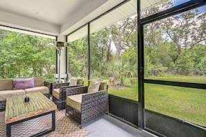 A covered outdoor seating area with wicker furniture, a coffee table, and a view of a grassy yard with trees. - 3 Mi to Usf: Dog-friendly Home w/ Large Yard (Lutz)