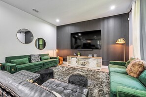 A modern living room with a green sofa, a leather couch, a TV, and a console table. - 3 Mi to Usf: Dog-friendly Home w/ Large Yard (Lutz)
