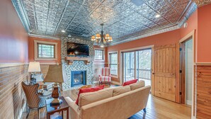 A spacious living room with a stone fireplace, a large sofa, and a wooden ceiling. - Mountain-view Georgia Cabin w/ 2 Decks (Dillard)