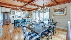 A spacious kitchen with wooden beams, a dining area with a large table, and a view through the windows. - Mountain-view Georgia Cabin w/ 2 Decks (Dillard)