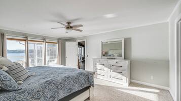 A bedroom with a large bed, a ceiling fan, a dresser, and a view of the outdoors.
