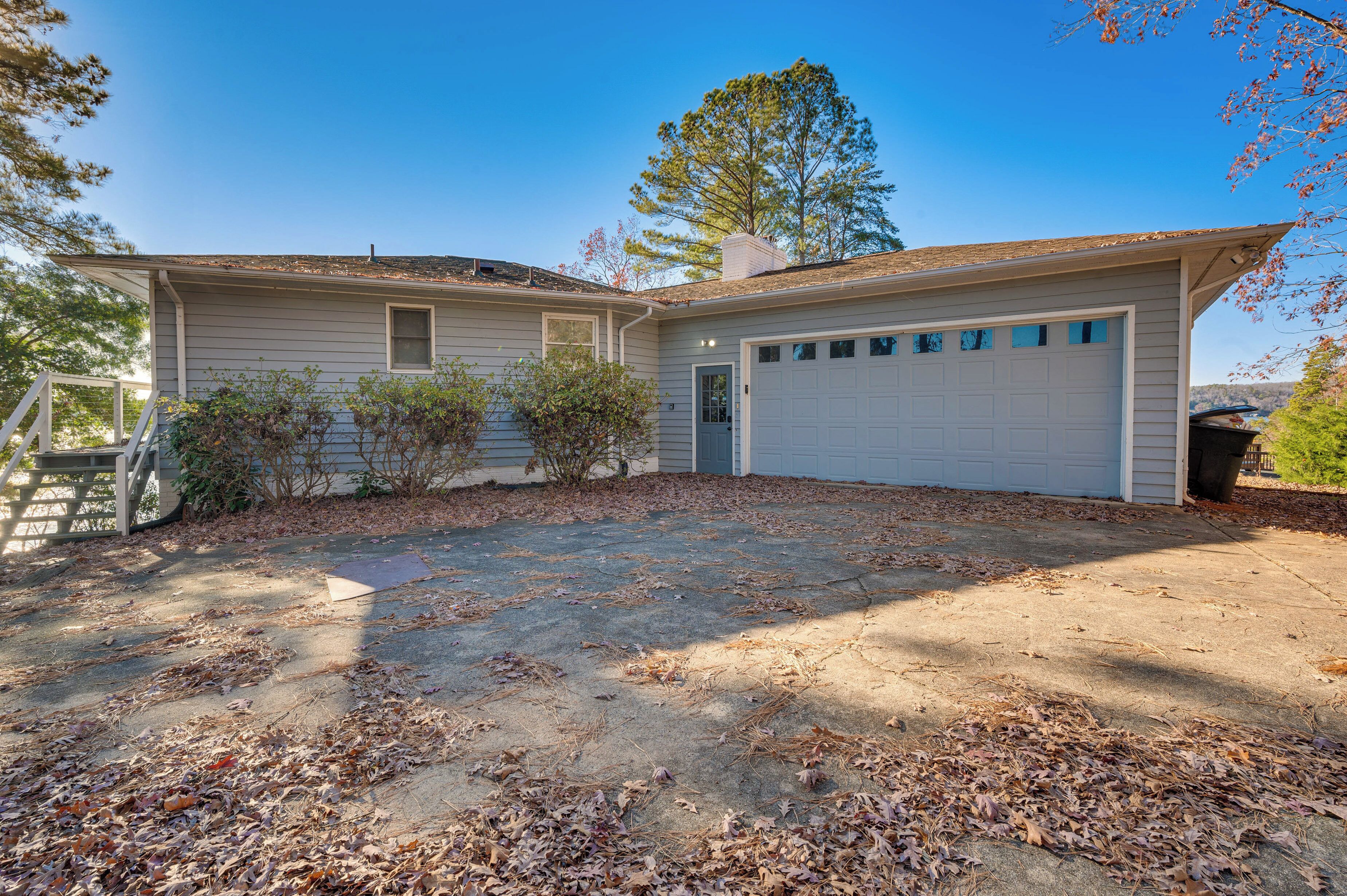 A single-story house with a garage, a front yard with scattered leaves, and a tree in the background.