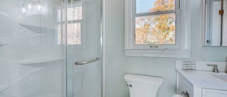 A bathroom with a glass shower enclosure, a toilet, and a sink with a mirror above.