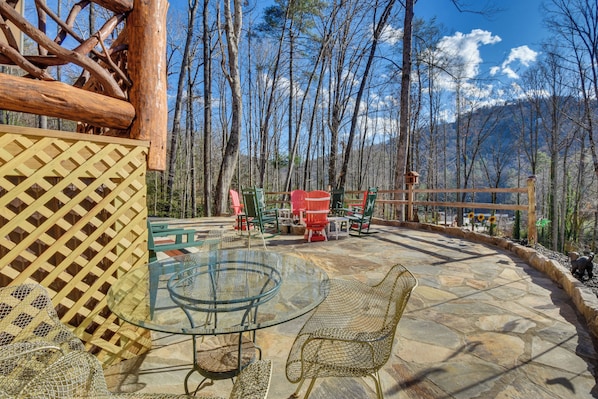 An outdoor patio with a glass table and wicker chairs, surrounded by a wooden fence and trees.