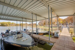 A covered boat dock with several boats moored, a dockside chair, and a water filtration system. - Grill & Dock Access: Waterfront Kerens Cabin (Kerens)