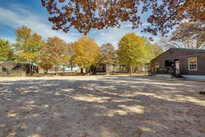 A campground with a dirt ground, trees with autumn leaves, and a wooden building with a green roof.