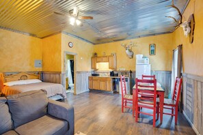 A room with a bed, a sofa, a dining table with chairs, a kitchen area, and a ceiling fan.