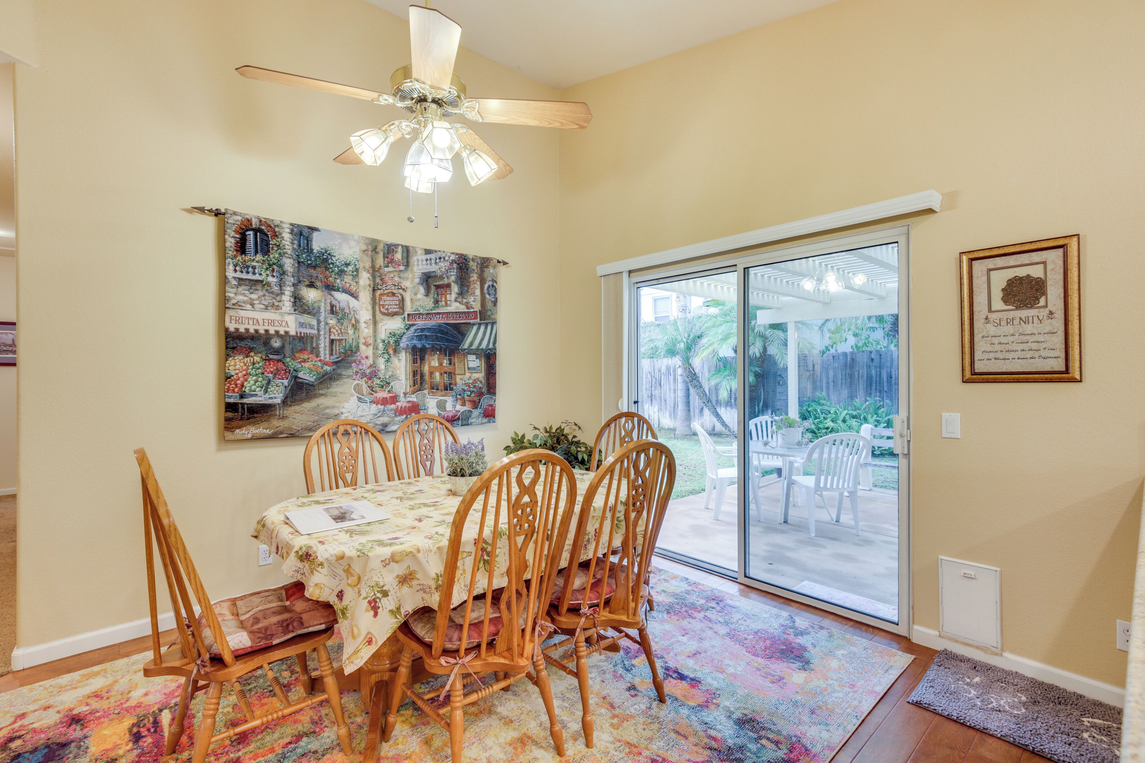 A dining area with a table set for six, wooden chairs, a ceiling fan, and a large window with a view of the backyard.
