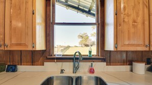 A kitchen with wooden cabinets, a double sink, a window with a view of a yard, and a digital clock.