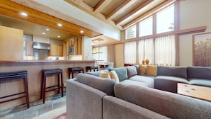 Una cocina moderna con armarios de madera y una barra, una sala de estar acogedora con un sofá seccional, y ventanas amplias que ofrecen luz natural.