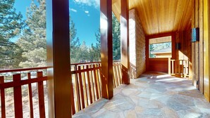 Interior de madera con suelo de piedra, barandilla de madera y vista a árboles.