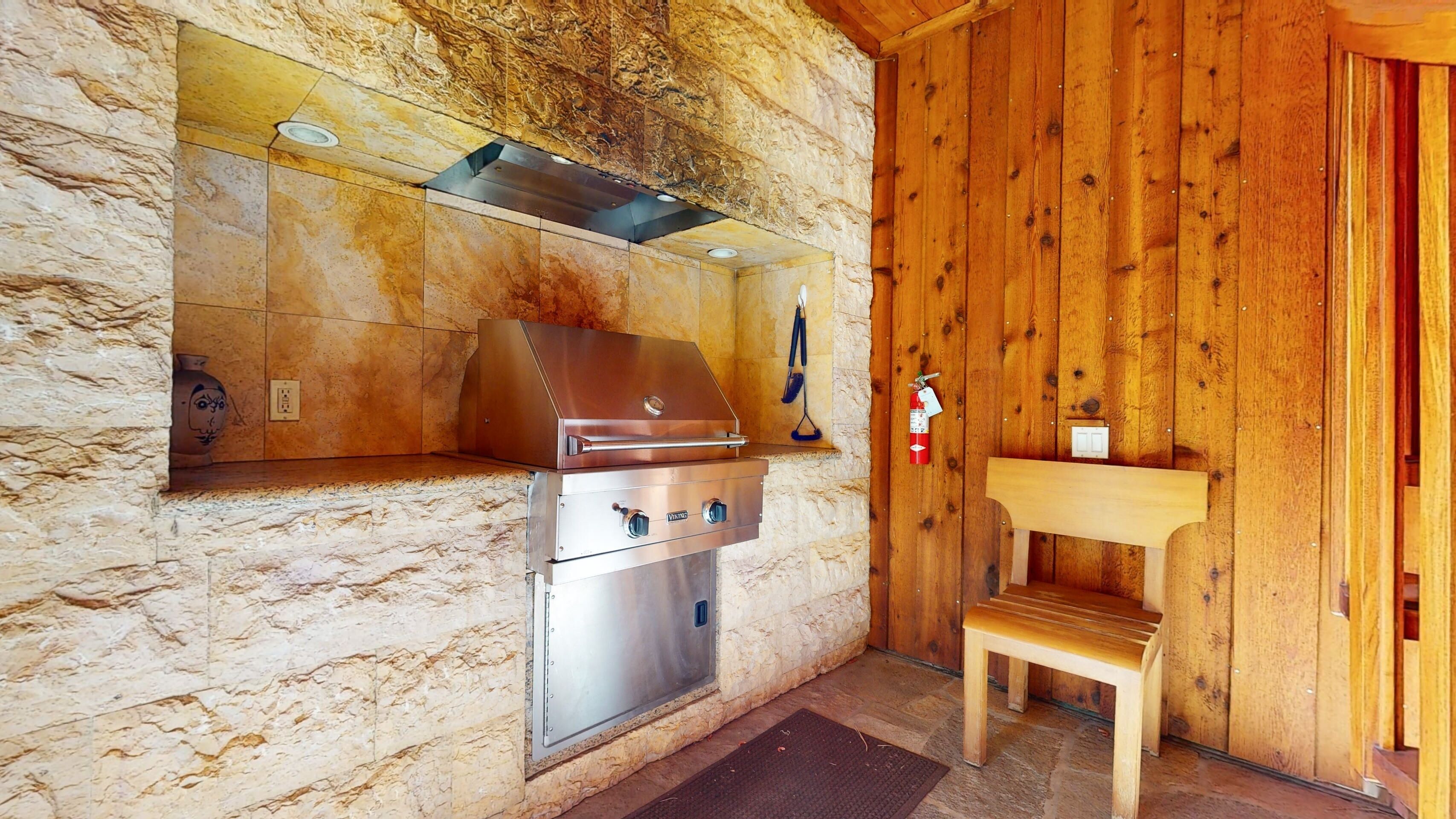 A stone-walled kitchen with a stainless steel grill and a wooden bench.