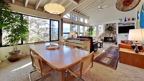 A spacious living area with a large wooden dining table, comfortable seating, a fireplace, and large windows offering natural light and views. - 1849 Condos 631 4 Bedroom Home by RedAwning (Mammoth Lakes)