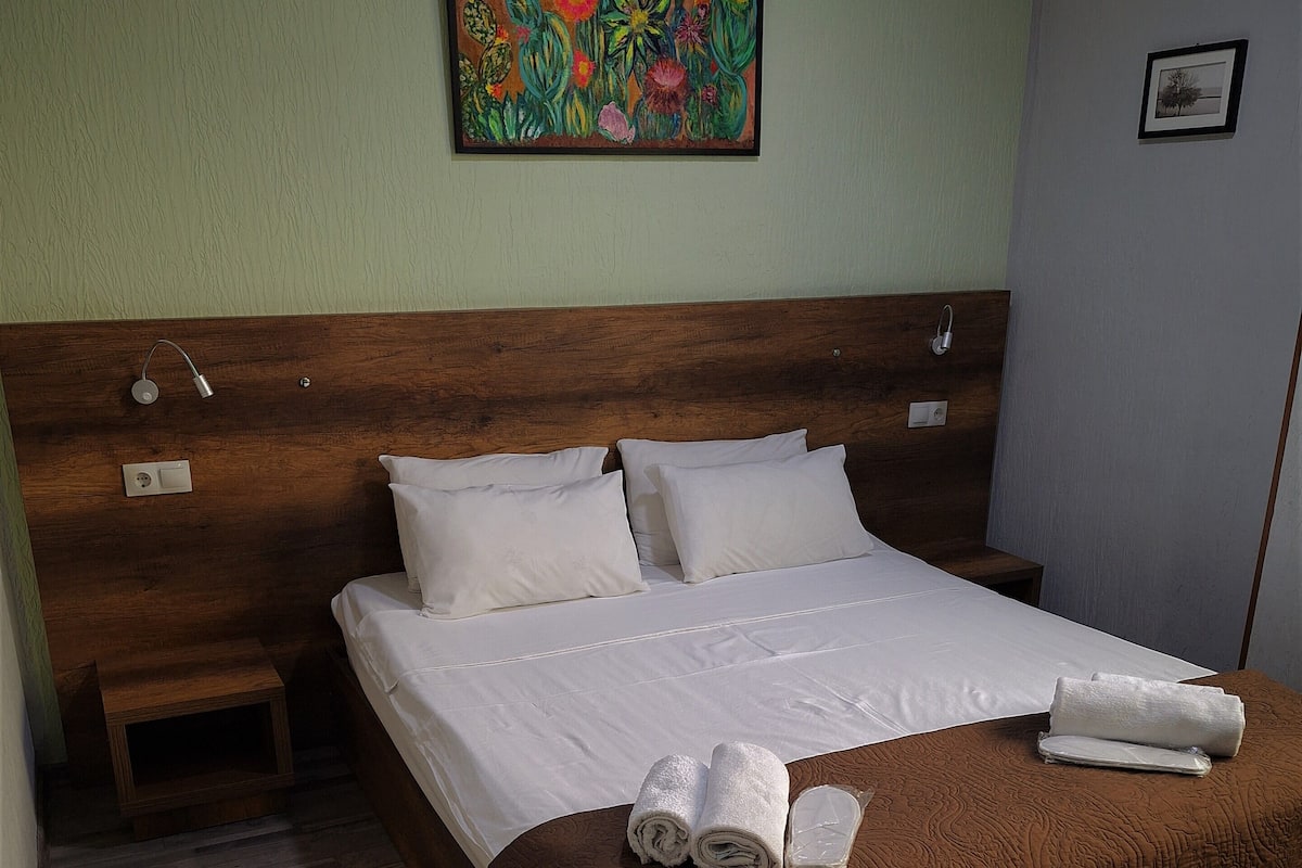 A neatly made bed with a brown headboard, a small bedside table, and a wall-mounted painting.