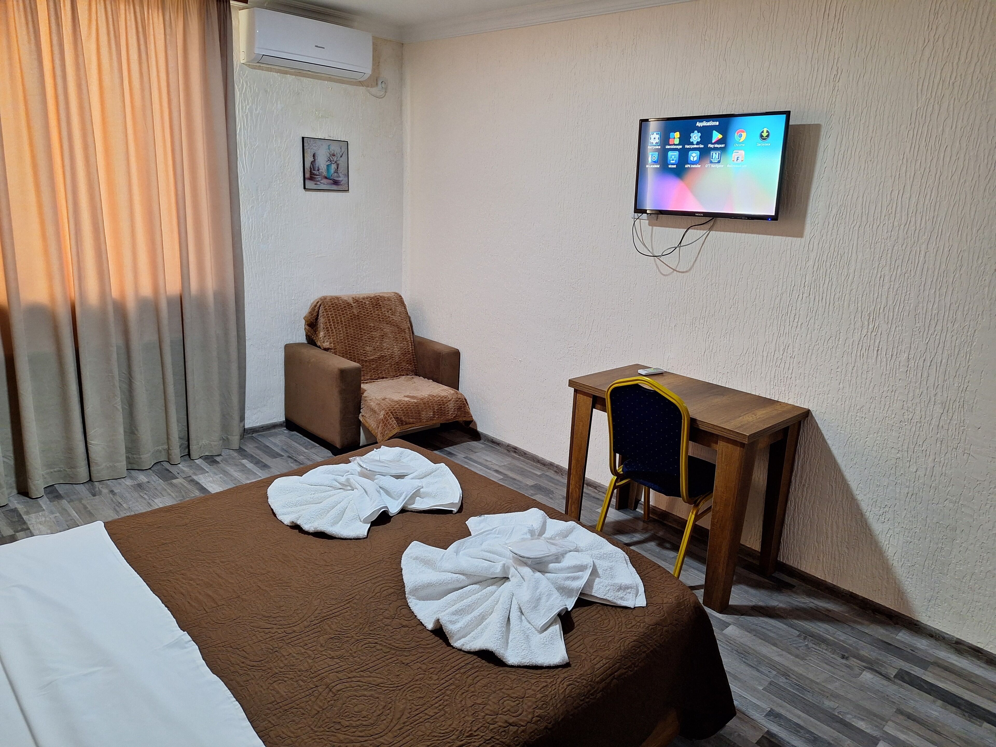 A hotel room with a bed, a chair, a small table, a TV, and an air conditioning unit.