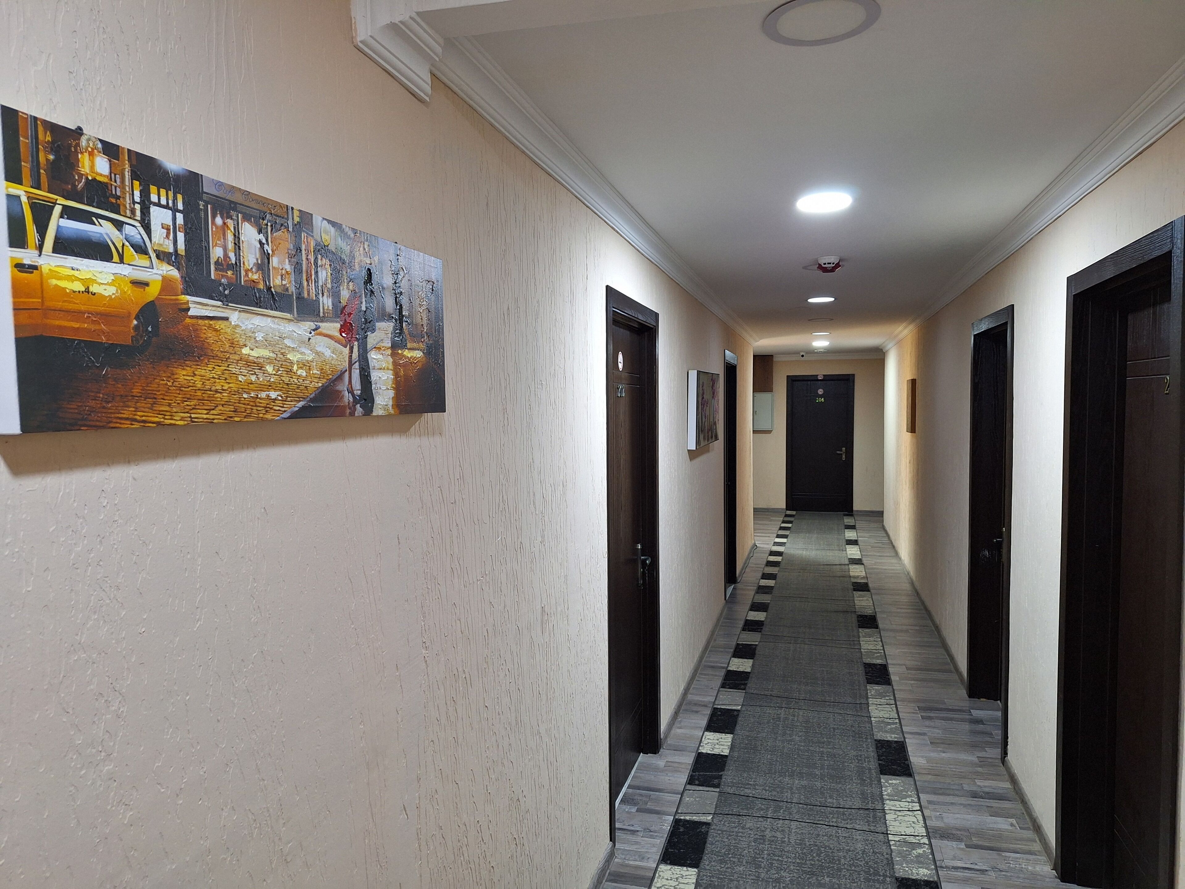 A hotel hallway with a checkered floor, a painting of a street scene, and a door with the number 204.