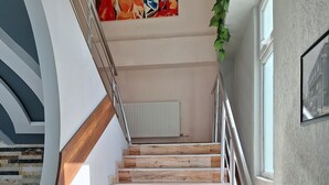 Una escalera de madera con barandillas de metal que conduce a un rellano con un radiador y un cuadro.