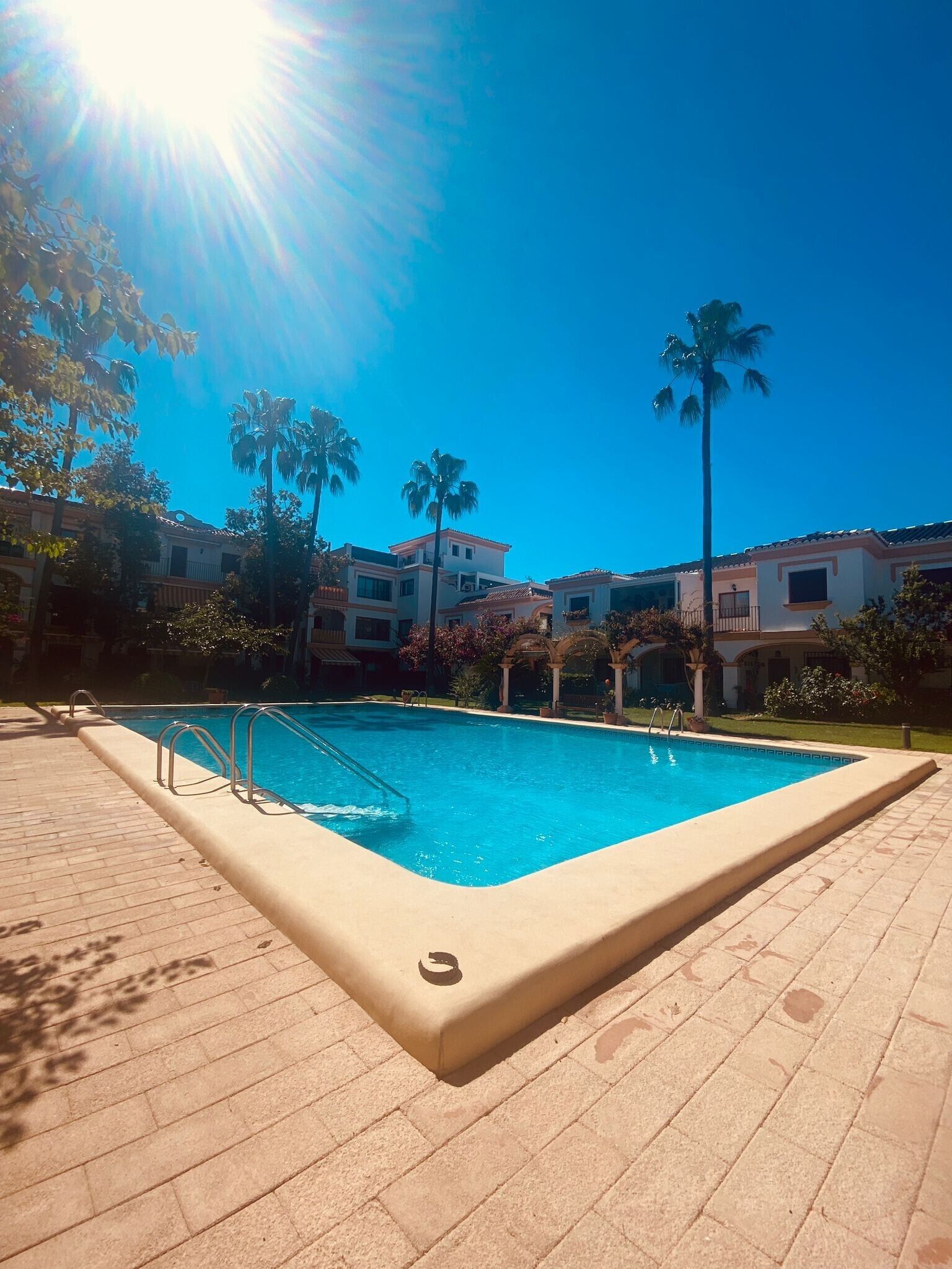 Ein Schwimmbad mit blauem Himmel, Palmen und Gebäuden im Hintergrund.