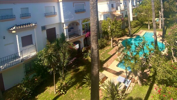 Zona residencial con piscina, palmeras y casas con balcones.