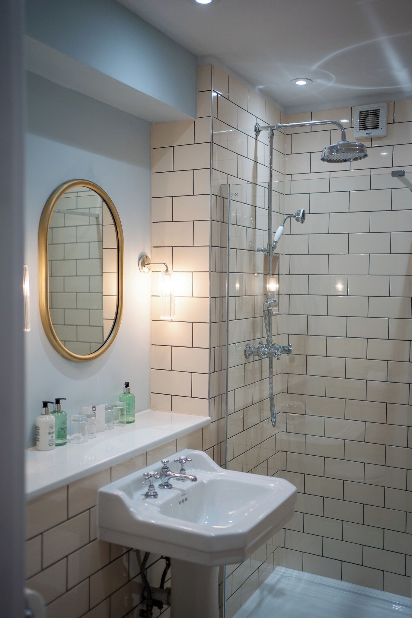 A modern bathroom with a glass-enclosed shower, a white sink, and a mirror with a gold frame.