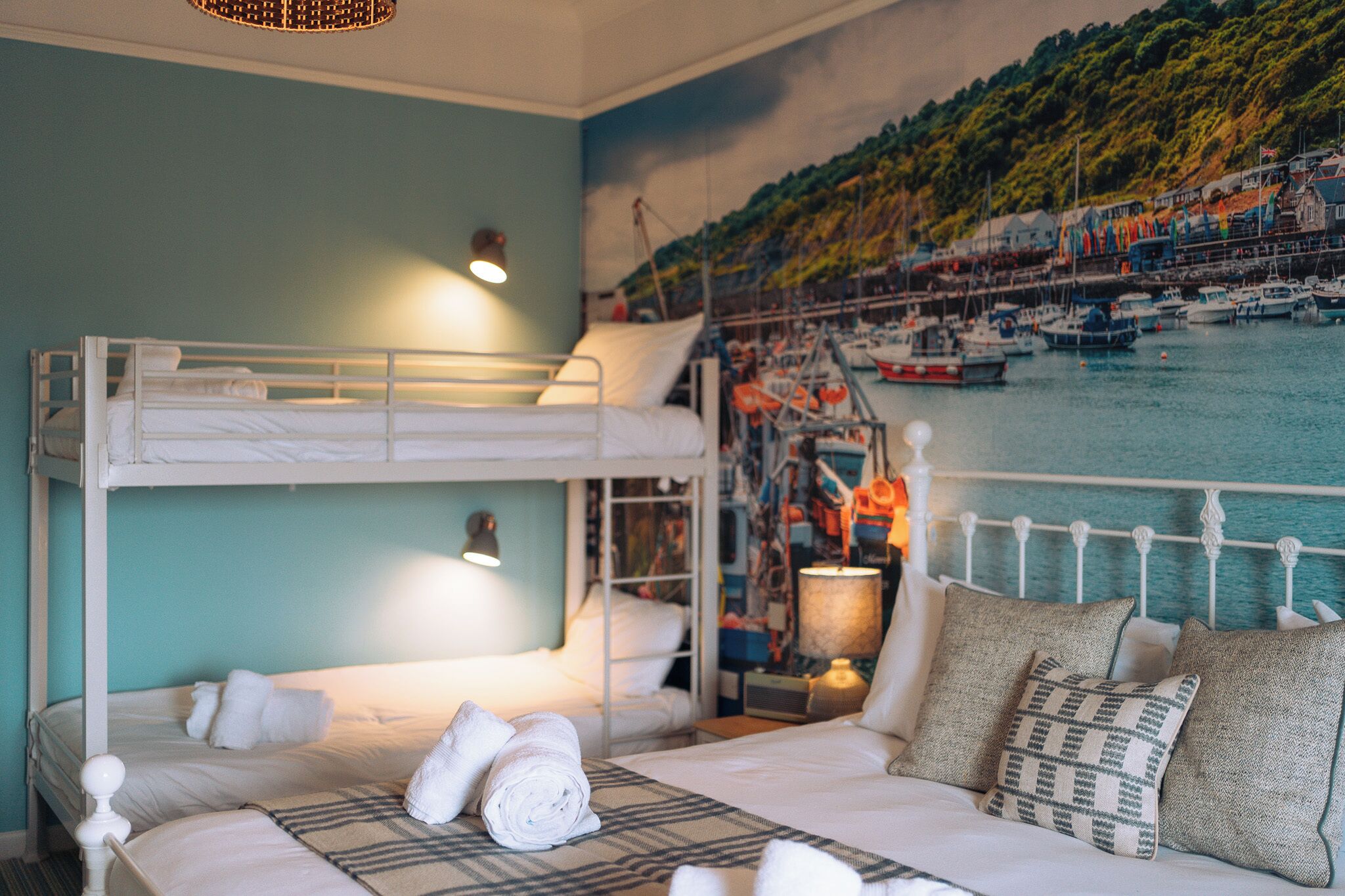 A room with bunk beds, a mural of a harbor, and a bed with a patterned throw.