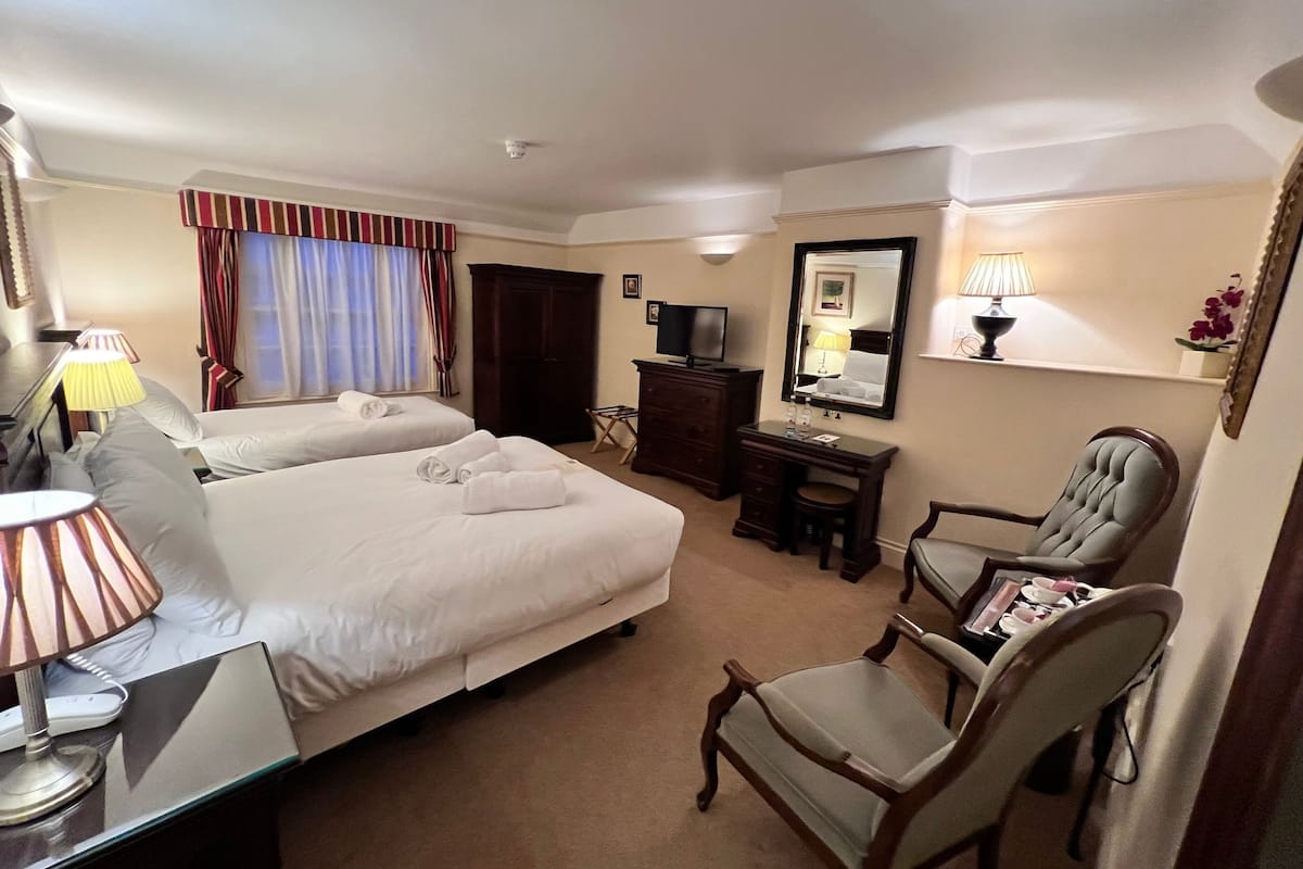 Une chambre d’hôtel avec deux lits, un bureau avec une lampe, une chaise, une commode, une télévision et un miroir au mur.