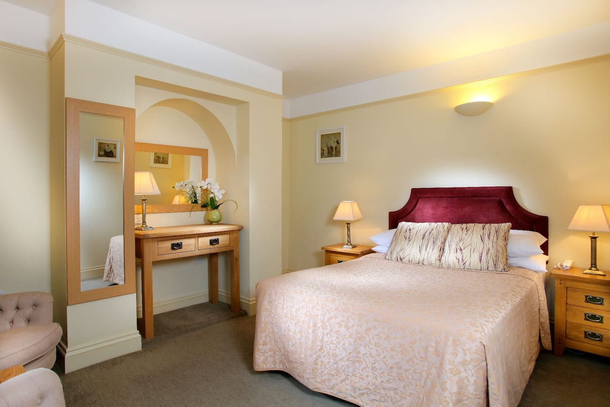 Une chambre d’hôtel avec un grand lit, une coiffeuse avec un miroir et deux tables de chevet avec des lampes.