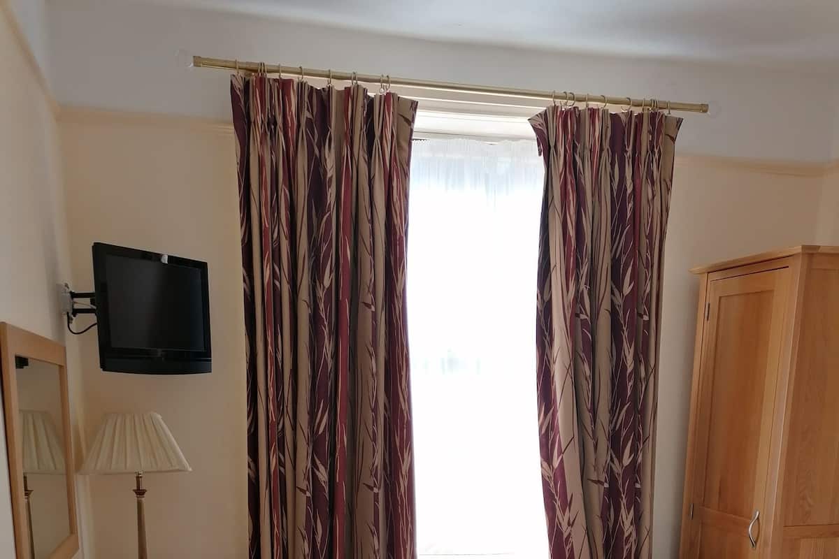 Une chambre d’hôtel comprenant un lit, un bureau avec une lampe, une chaise, une armoire et un téléviseur fixé au mur.