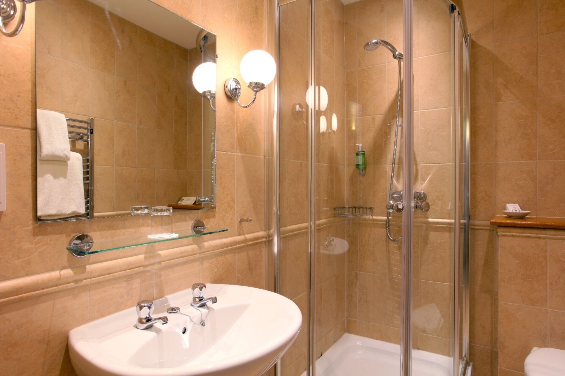 A modern bathroom with a glass-enclosed shower, a white sink with two faucets, and a large mirror.