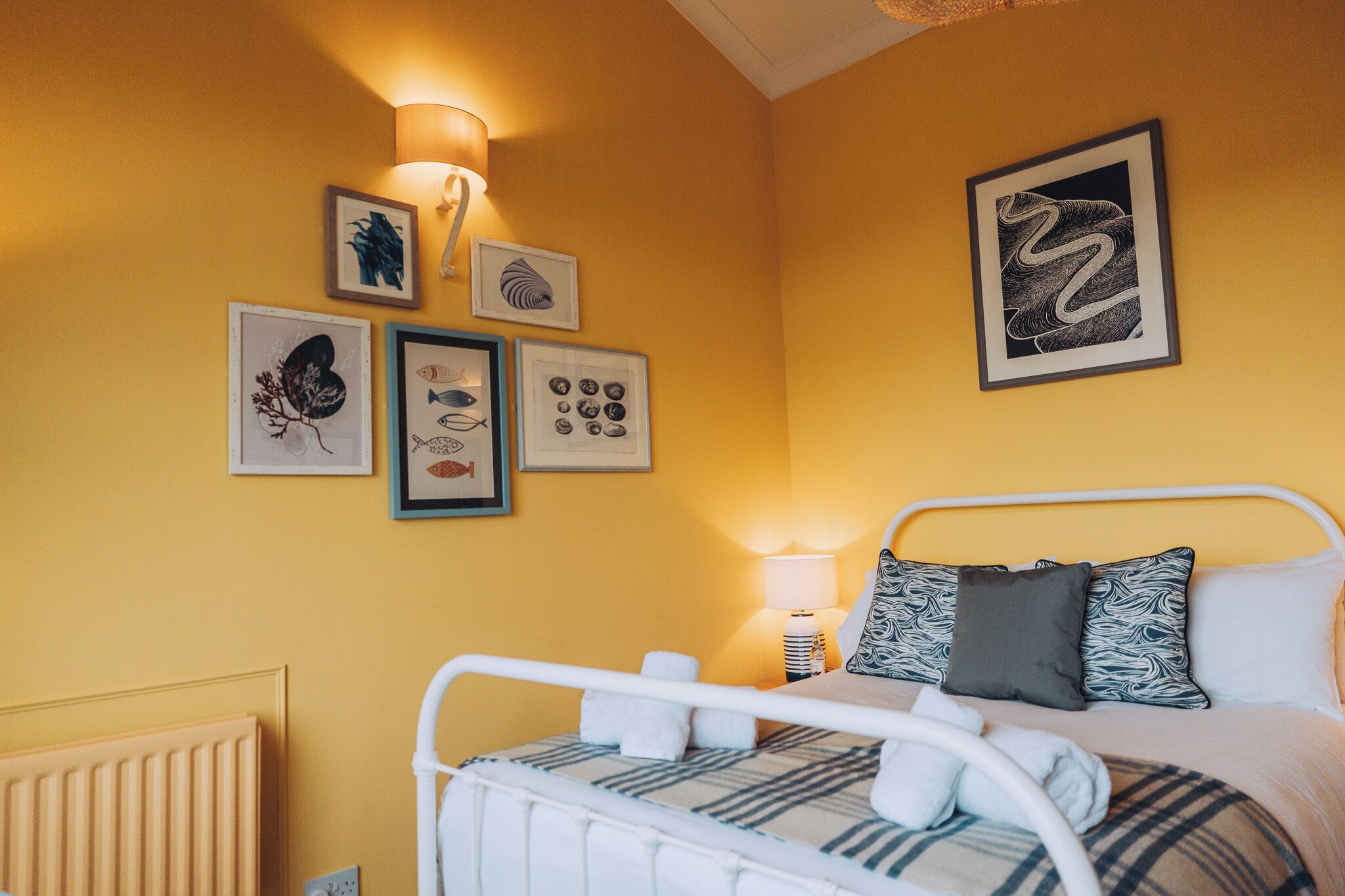 A bedroom with a bed, wall-mounted artwork, and a bedside lamp.