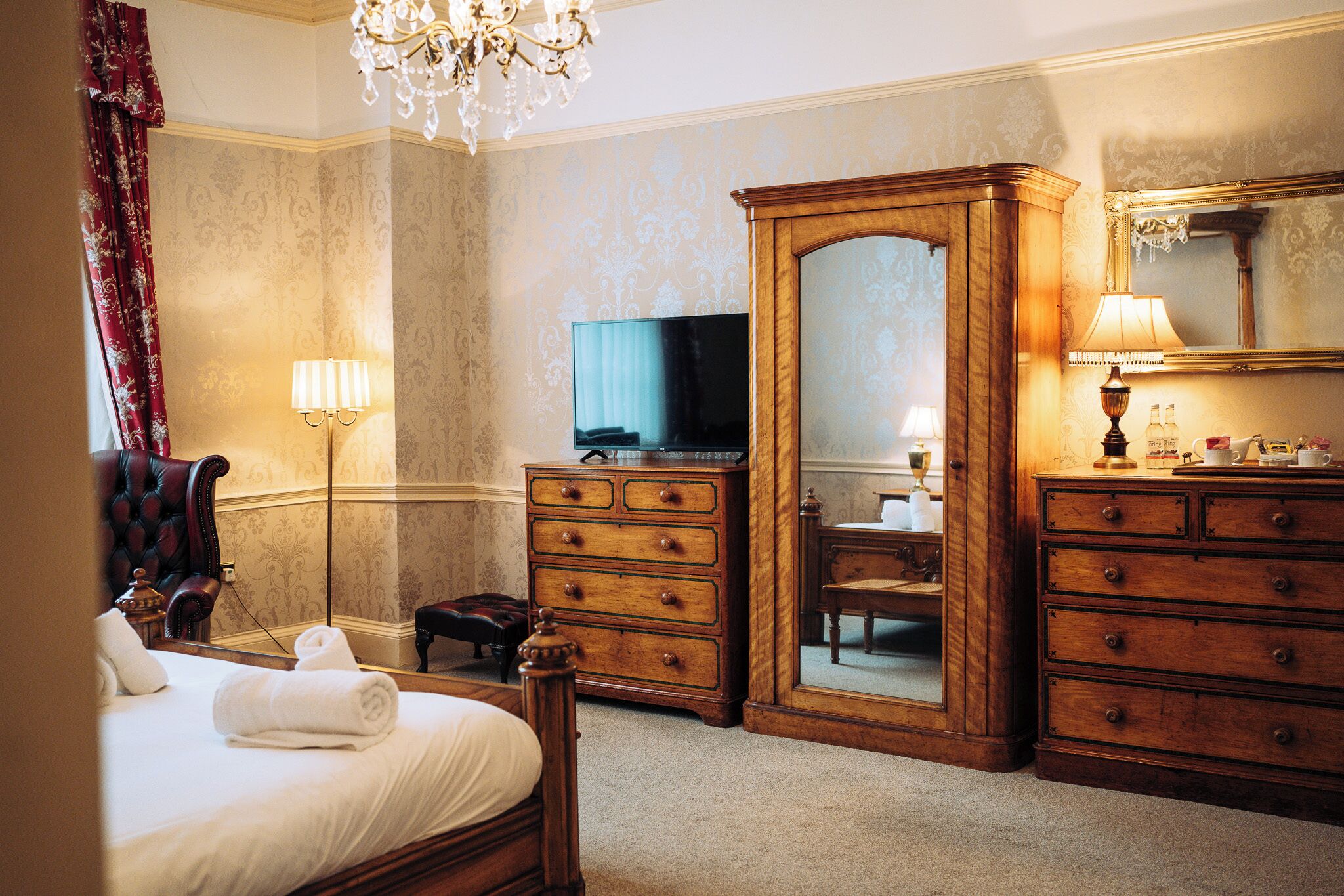 A hotel room with a bed, a television, a large mirror, and wooden furniture.