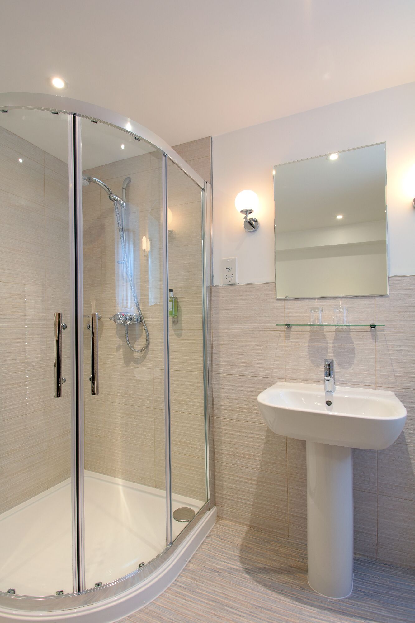 A modern bathroom with a glass-enclosed shower, a white sink, and a mirror above it.