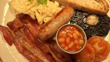 A plate with bacon, sausages, toast, scrambled eggs, baked beans, and tomatoes.
