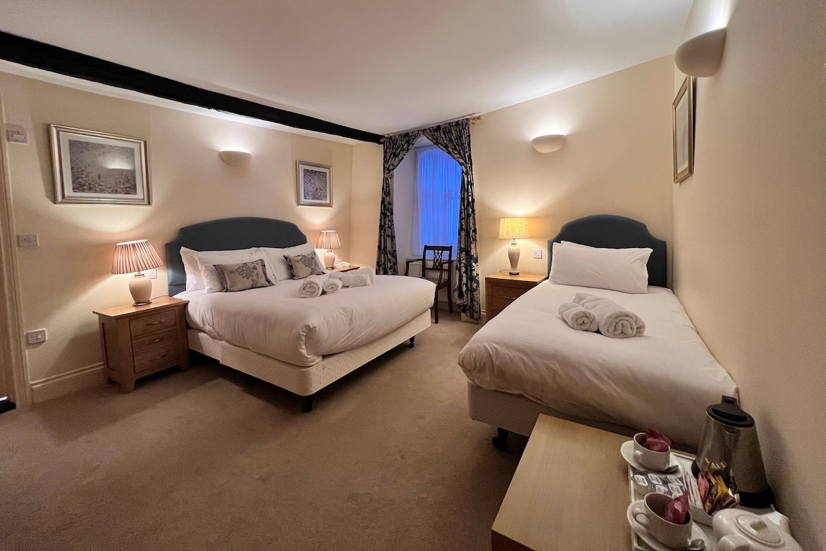 Une chambre d’hôtel avec deux lits, une petite table avec une machine à café et une chaise.